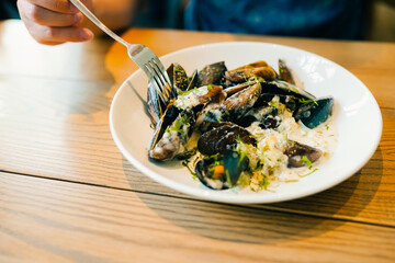 Steamed mussles in white bowl on table with hands