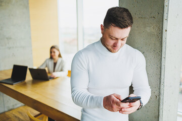 Successful male businessman in casual clothes smiling looking at phone standing in modern light office with phone working in modern company.