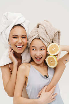 Two smiling women hugging while posing with lemon isolated over white background