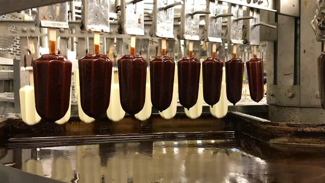 Confectionery production. Ice cream machine dips into chocolate. Food factory.