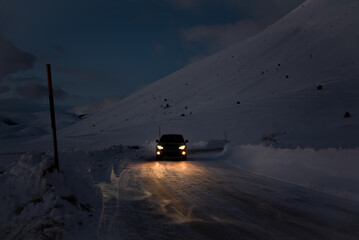 Car driving on winter road in dark surrounded by mountains covered with snow