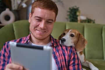 Unwind with your four-legged friend: a man and his Beagle lounging on the couch as he catches up on current events and shares a moment of bonding