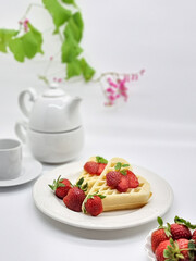 Selective focus of Waffles garnished with strawberries on a white plate with white background