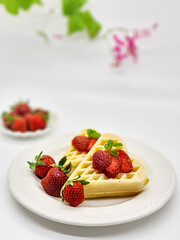 Selective focus of Waffles garnished with strawberries on a white plate with white background