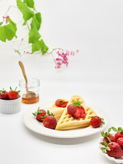 Selective focus of Waffles garnished with strawberries on a white plate with white background