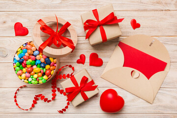 Red envelope with candy and gift box and Valentines hearts on colored background. Flat lay, top view. Romantic love letter for Holiday concept
