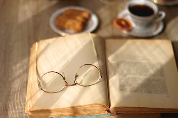 Cup of tea, plates with cookies, glass of orange juice, books, reading glasses, bowl of fruit and candles on the table. Selective focus.
