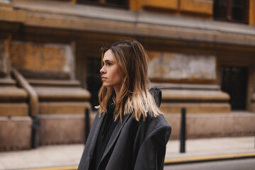 Fototapeta premium Photo of cute charming young woman wear grey jacket, calm walking outside city street. Girl look at side.