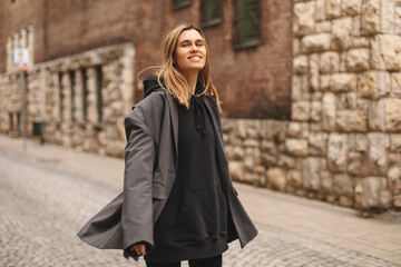 Young beautiful smiling hipster woman in trendy outfit. Sexy carefree woman posing on the street. Cheerful and happy girl wear grey suit and black hoodie turn around. Lifestyle, female beauty concept.