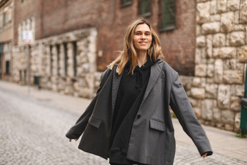 Fototapeta premium Young beautiful smiling hipster woman in trendy outfit. Sexy carefree woman posing on the street. Cheerful and happy girl wear grey suit and black hoodie turn around. Lifestyle, female beauty concept.