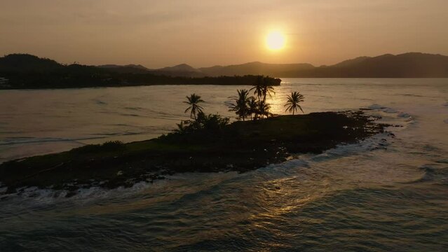 Small tropical island surrounded by ocean waves, golden hour aerial, sunrise