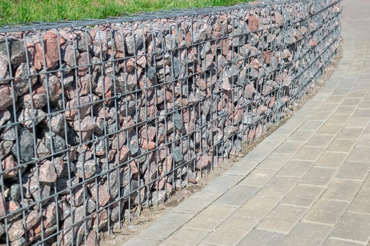 Decoration Of The Sidewalk Path With A Metal Mesh With Natural Stone, Gravel. Landscaping Of The Area. A Patch Of Lawn At The Top