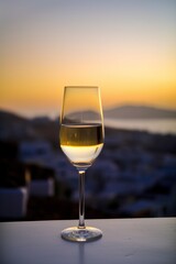 Obraz premium Glass of white wine on balcony with sunset view over Mediterranean island, AI generative