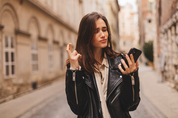 Fototapeta premium Portrait of wishful young woman in casual clothes with brunette hair, crossing her fingers, feeling nervous before important event, walking on the street. Body language.