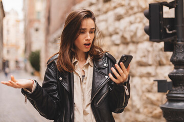 Explain wtf message mean. Portrait of frustrated questioned and annoyed young woman arguing over bad news shrugging spread hands in dismay sideways being displeased walking on the street in city.