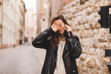 Sad woman checking bad news on mobile phone complaining alone in the street. Upset young woman thinking about her problems. Girl cover her face by her hand. Negative, bad news, breakup, unhappy.