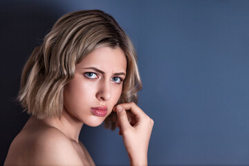 Close up portrait frowning woman, posing at dark gray background, looking at camera. Emotional face of lovely young blond lady isolated on blank studio wall. Human emotions concept. Copy ad text space