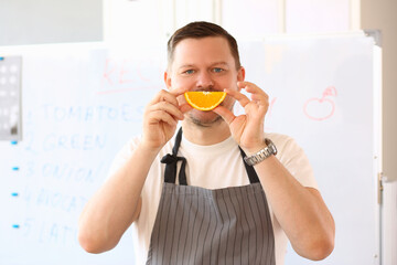Emotionally smiling male cook holds an orange slice together smiles
