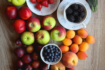 Berries in vintage porcelain dishes, other healthy fruit and vegetable on wooden table. Top view.