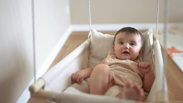 baby is swinging on a swing. baby blonde play at home sits on a rope swing. happy family kid dream kindergarten concept. pov view of baby playing in baby lifestyle swing indoors