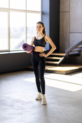 Fototapeta premium Attractive healthy young woman with a fitness mat at the yoga studio