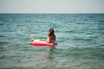 Young sexy woman in a slender body in a white swimsuit next to an inflatable mattress. Summer holidays. Rest on the sea. The concept of a healthy lifestyle.
The girl is resting on the sea. 