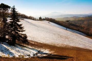 Countryside landscape in autumn with snow, agricultural fields among hills