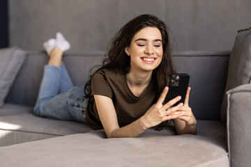 Happy woman relaxing on comfortable sofa, enjoying web surfing information in internet or using mobile software application, communicating distantly with friends in social networks at home.