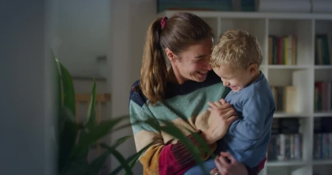Young Playful Woman Holding her Male Toddler in her Arms and Dancing with Him in the Living Room at Home. Little Cute Boy and his Energetic Mother Having Fun, Bonding, Laughing