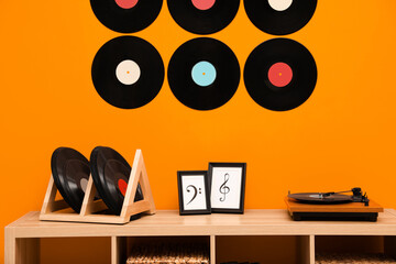 Vinyl records and player on wooden cabinet near orange wall