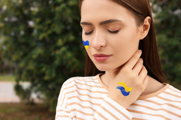 Young woman with drawings of Ukrainian flag outdoors, closeup. Space for text