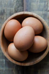 Many chicken eggs in a wooden bowl on burlap on a wooden background. Rustic style. The concept of organic food. Vertical orientation. Top view.