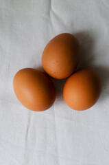 Three chicken eggs on a white tablecloth. Rustic style. The concept of organic food. Minimalism. Vertical orientation. Copy space. Top view