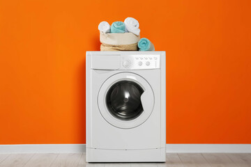 Washing machine with clean towels near orange wall indoors. Interior design