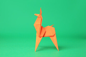 Origami art. Handmade orange paper deer on green background