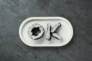 Word Ok made of sushi rolls on dark grey table, top view
