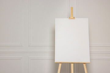 Wooden easel with blank canvas near white wall. Space for text