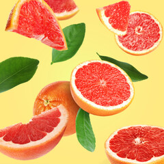 Cut fresh grapefruits and green leaves flying on light yellow background