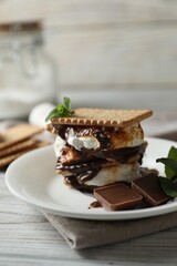 Delicious marshmallow sandwich with cracker and chocolate on white wooden table, closeup