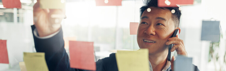 Businessman writing on sticky notes on glass wall while working in modern office