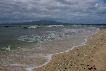 Sandy beach of a tropical island. Overcast weather. Sea wave rolls on the sandy beach.