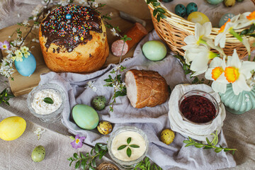 Traditional Easter food. Homemade easter bread, natural dyed easter eggs, ham, beets, butter, cheese on linen napkin on rustic table with spring flowers. Top view.