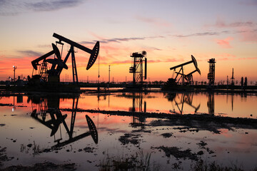 in the evening, oil pumps are running, The oil pump and the beautiful sunset reflected in the water, the silhouette of the beam pumping unit in the evening.