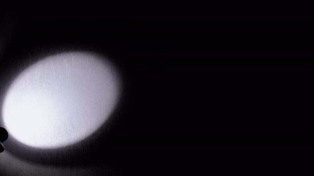 Unrecognizable Person Shines a Flashlight on the Wall in a Dark Room. Close-up. Silhouette of a hand with a flashlight illuminates the wall in dark. Spot or beam of light from a lantern. Shadow.