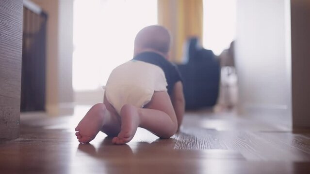 baby learns to crawl on the floor at home. happy family kindergarten kids concept. First steps, baby crawling view from the back. baby learns to crawl to explore the world dream around him