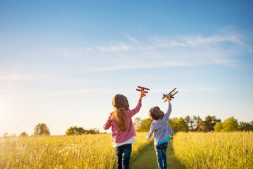 Boy and girl plaing with wooden planes on the field in sunset - obrazy, fototapety, plakaty