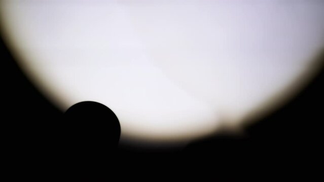 Unrecognizable Person Shines a Flashlight on the Wall in a Dark Room. Close-up. Silhouette of a pocket flashlight illuminates the wall in the dark. Spot or beam of light from a lantern. Shadow. 4K.