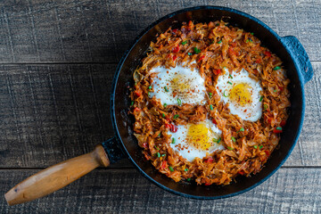 Stewed cabbage with vegetables and fried eggs in a frying pan on a wooden background, closeup, top view. Food background. Healthy food