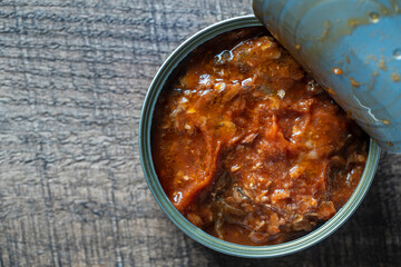 Open canned sardines in tomato sauce on a wooden background, closeup, top view, copy space