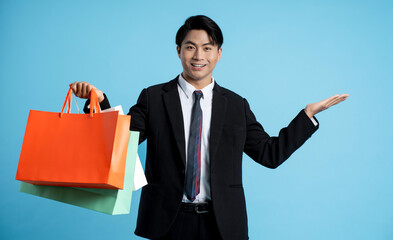 Portrait of young businessman holding shopping bag on blue background